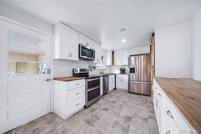 kitchen featuring stainless steel appliances, butcher block counters, decorative backsplash, and white cabinets