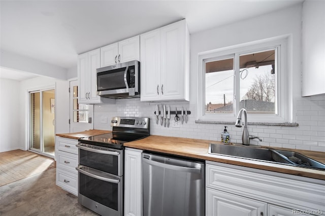 kitchen featuring appliances with stainless steel finishes, butcher block countertops, white cabinetry, sink, and backsplash