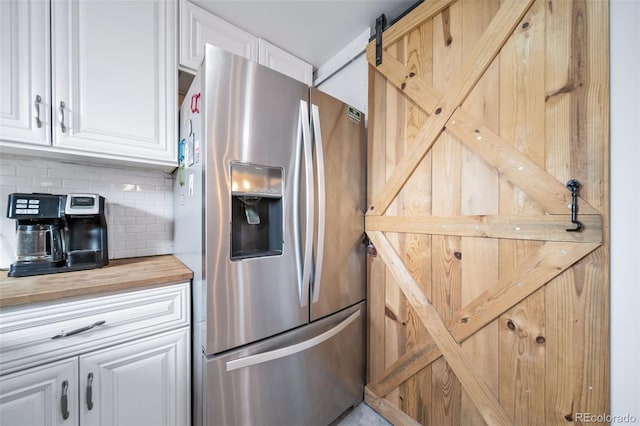 kitchen featuring tasteful backsplash, stainless steel refrigerator with ice dispenser, a barn door, and white cabinets