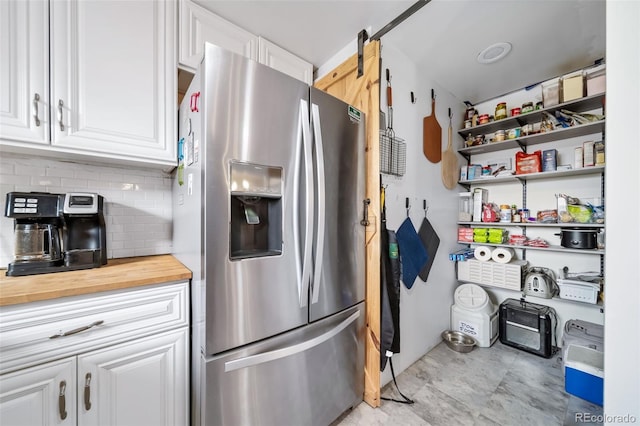 kitchen featuring tasteful backsplash, stainless steel fridge, a barn door, and white cabinets