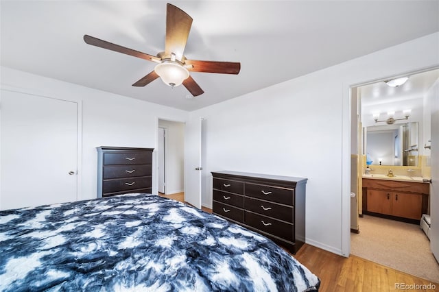 bedroom featuring ceiling fan, ensuite bathroom, light hardwood / wood-style flooring, and a baseboard heating unit