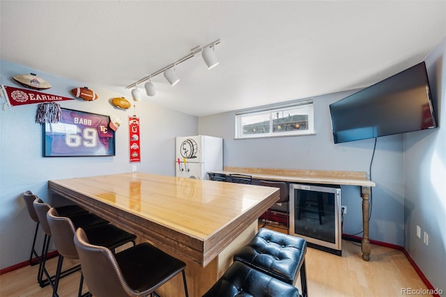 bar featuring light hardwood / wood-style flooring, track lighting, beverage cooler, and white fridge