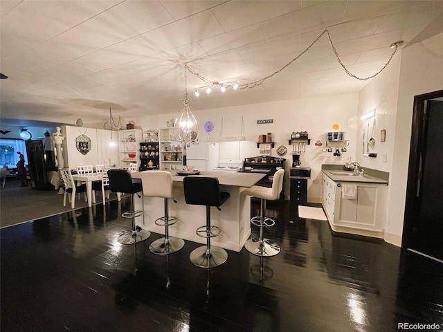 kitchen featuring a sink, freestanding refrigerator, white cabinetry, dark wood-type flooring, and a breakfast bar area