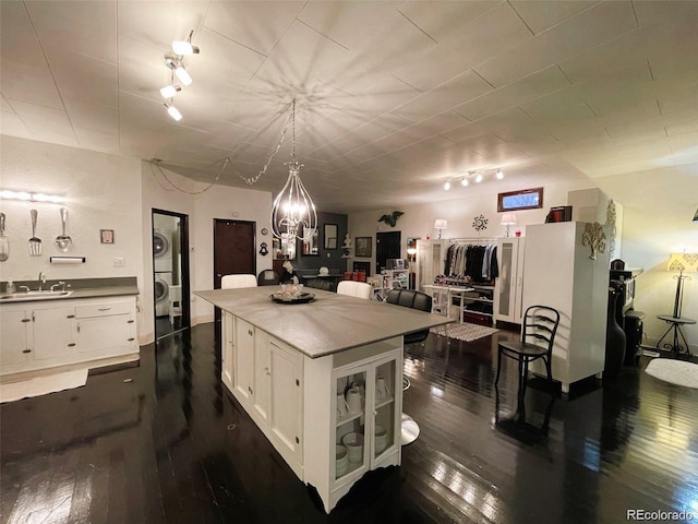 kitchen featuring a sink, track lighting, stacked washer / drying machine, white cabinets, and dark wood-style flooring
