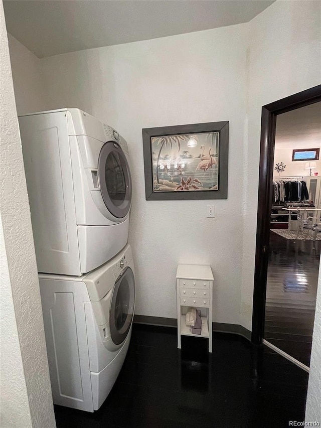 laundry room featuring stacked washer and clothes dryer, wood finished floors, baseboards, and laundry area