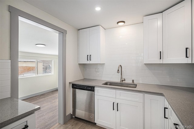 kitchen with sink, white cabinetry, light hardwood / wood-style flooring, stainless steel dishwasher, and backsplash