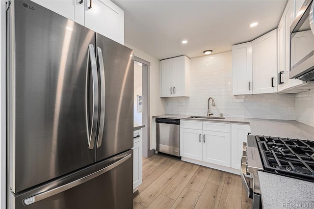 kitchen with tasteful backsplash, white cabinets, light wood-style flooring, stainless steel appliances, and a sink