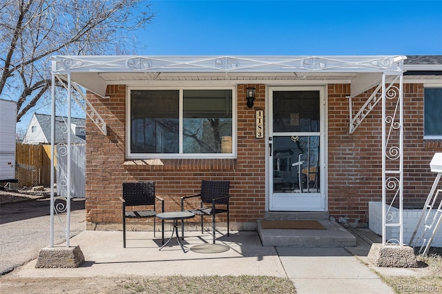 view of exterior entry featuring fence, a patio, and brick siding