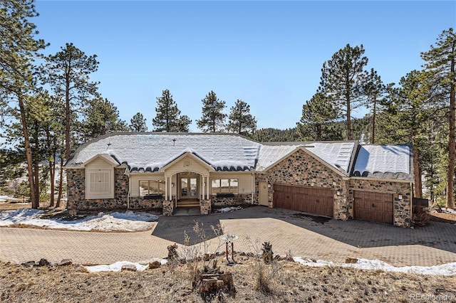 view of front of house with a garage, stone siding, decorative driveway, and french doors