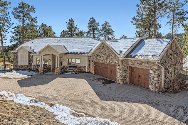 view of front of house with covered porch, stone siding, decorative driveway, and an attached garage