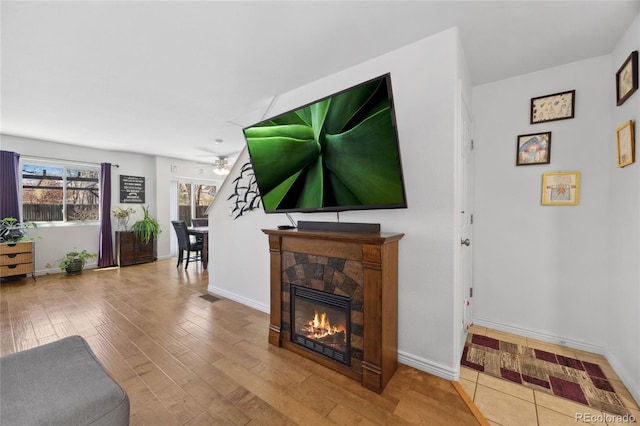 living area featuring ceiling fan, wood finished floors, a glass covered fireplace, and baseboards