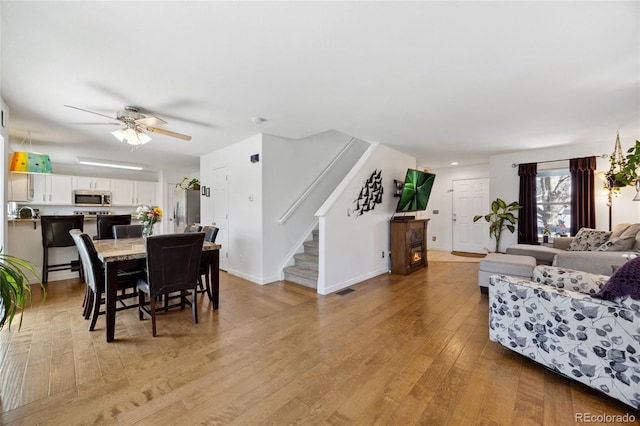 living area featuring stairway, light wood finished floors, ceiling fan, and baseboards