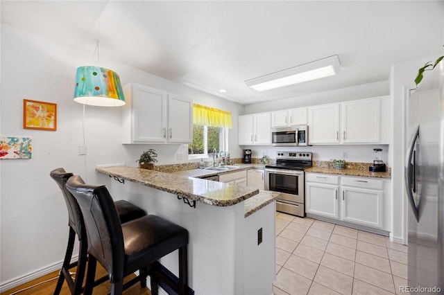 kitchen with appliances with stainless steel finishes, a peninsula, white cabinetry, a sink, and a kitchen bar