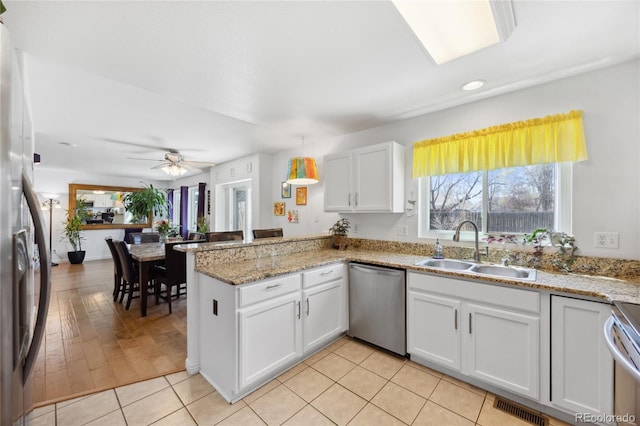 kitchen featuring appliances with stainless steel finishes, a sink, a peninsula, white cabinetry, and a ceiling fan