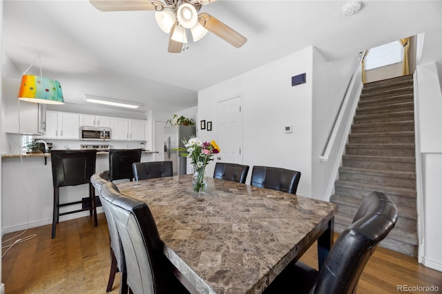 dining area featuring a ceiling fan, wood finished floors, and stairway