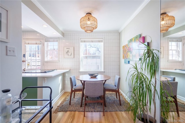 dining space with light wood-style floors, crown molding, tile walls, and baseboards