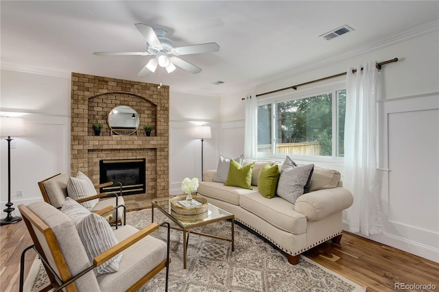 living room with ceiling fan, ornamental molding, a brick fireplace, and light wood-type flooring