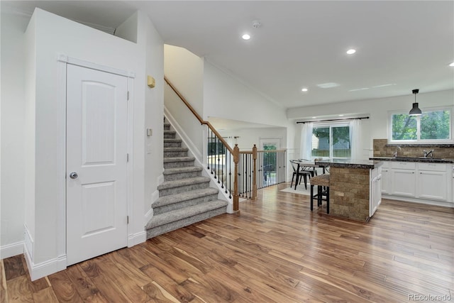 kitchen featuring hanging light fixtures, a breakfast bar, vaulted ceiling, light wood-type flooring, and white cabinetry