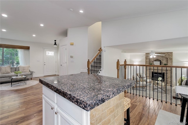 kitchen featuring light wood-type flooring, a kitchen island, a brick fireplace, ceiling fan, and white cabinets