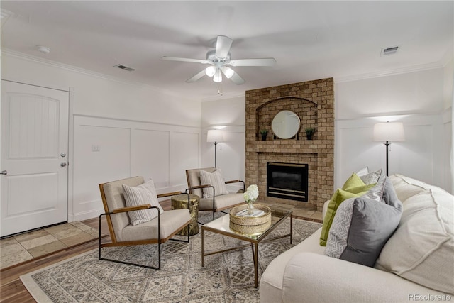 living room with crown molding, a brick fireplace, wood-type flooring, and ceiling fan