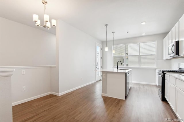 kitchen with dark wood-type flooring, white cabinets, an island with sink, decorative light fixtures, and stainless steel appliances