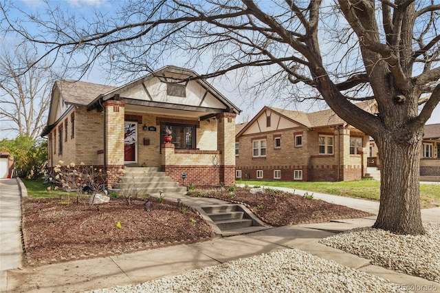 tudor house with a porch, a shingled roof, and brick siding
