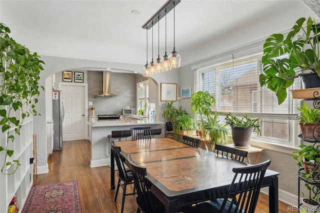 dining space with arched walkways, wood finished floors, and baseboards