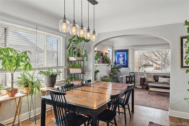 dining room with a textured wall, baseboards, arched walkways, and wood finished floors
