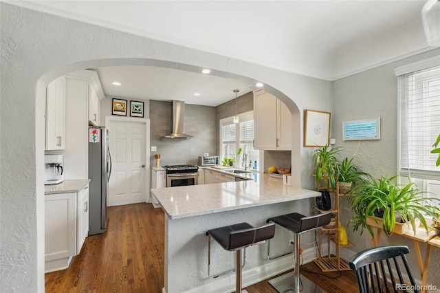kitchen with arched walkways, wall chimney exhaust hood, a peninsula, and stainless steel appliances