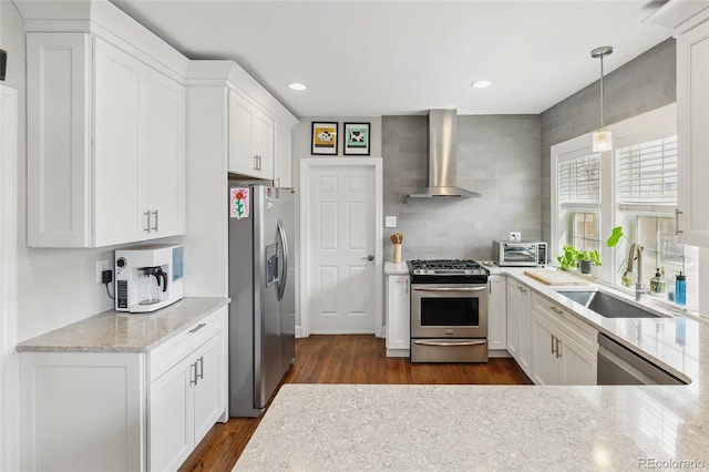 kitchen with white cabinets, a sink, wall chimney range hood, appliances with stainless steel finishes, and decorative backsplash