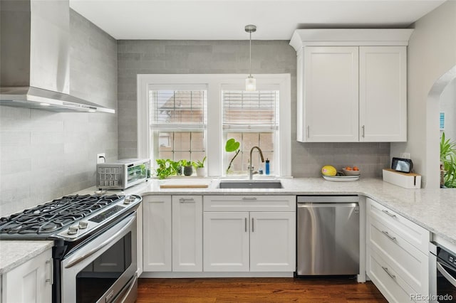 kitchen featuring white cabinets, a sink, wall chimney range hood, stainless steel appliances, and a toaster