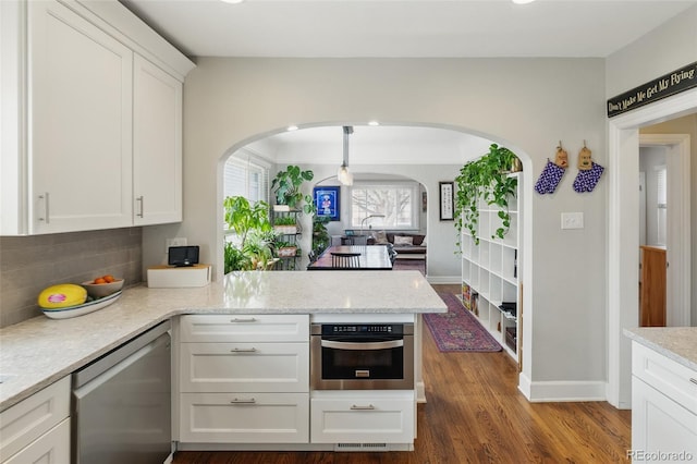 kitchen featuring white cabinets, arched walkways, a peninsula, stainless steel appliances, and decorative backsplash
