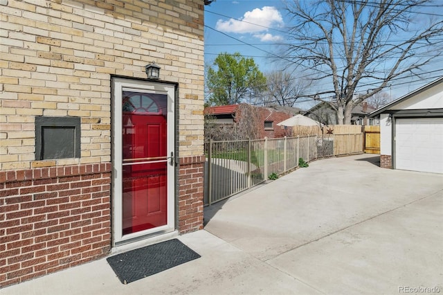 doorway to property with concrete driveway, fence, and brick siding