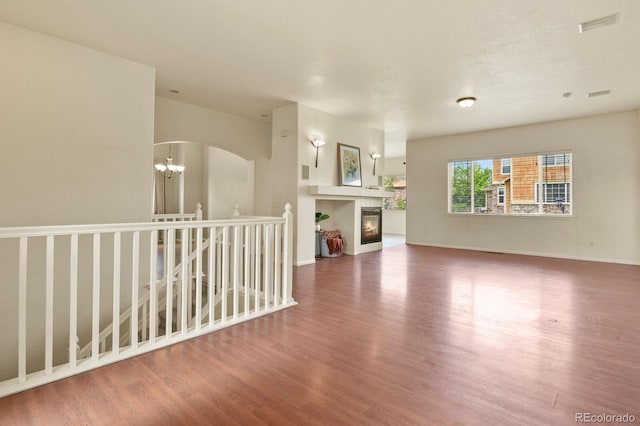 297 N Coolidge Way, Aurora, CO 80018 - unfurnished living room with wood finished floors, arched walkways, a glass covered fireplace, a chandelier, and baseboards