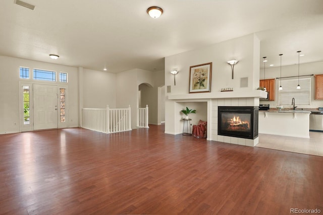 297 N Coolidge Way, Aurora, CO 80018 - unfurnished living room with a sink, arched walkways, wood finished floors, a tiled fireplace, and baseboards