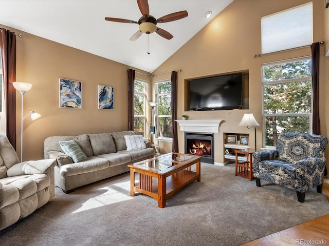 living room with a ceiling fan, healthy amount of natural light, a lit fireplace, high vaulted ceiling, and baseboards