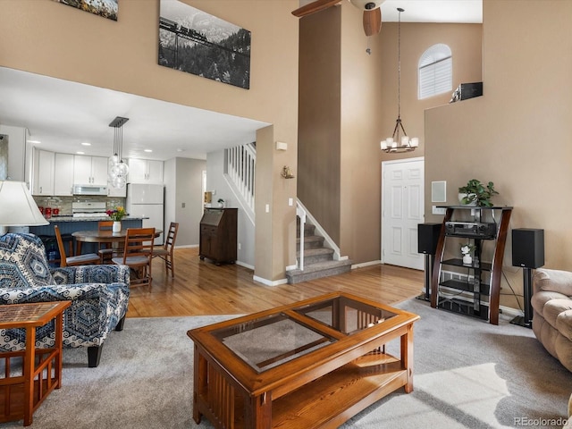 living area with a chandelier, a towering ceiling, stairs, light wood finished floors, and baseboards
