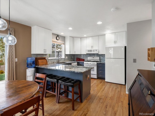 kitchen with white appliances, a peninsula, white cabinets, decorative backsplash, and a sink