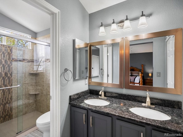 ensuite bathroom featuring a stall shower, double vanity, vaulted ceiling, toilet, and a textured wall
