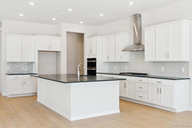 kitchen featuring sink, stainless steel gas cooktop, an island with sink, wall chimney range hood, and white cabinets