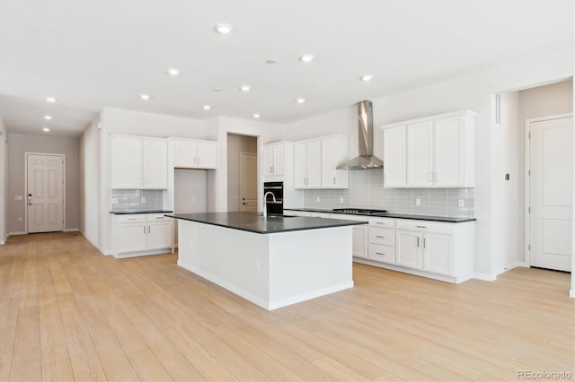 kitchen featuring a center island with sink, wall chimney range hood, white cabinets, and stainless steel gas stovetop