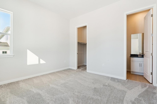 unfurnished bedroom with ensuite bathroom, a walk in closet, and light colored carpet