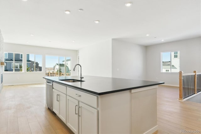 kitchen featuring white cabinetry, sink, stainless steel dishwasher, a center island with sink, and light hardwood / wood-style flooring