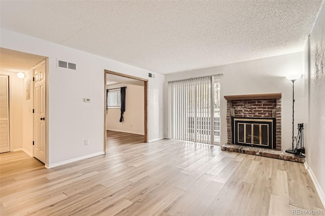 unfurnished living room with a brick fireplace, a textured ceiling, and light wood-type flooring