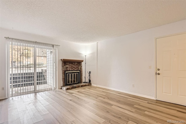 unfurnished living room with a textured ceiling, light hardwood / wood-style floors, and a brick fireplace