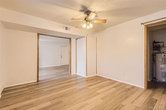 interior space with a textured ceiling, water heater, ceiling fan, and light hardwood / wood-style flooring