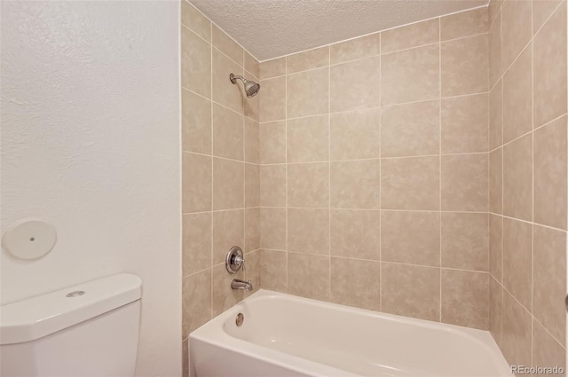 bathroom with a textured ceiling, tiled shower / bath combo, and toilet