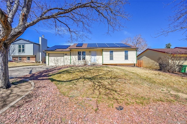 view of front of house with fence, driveway, solar panels, a front lawn, and a garage