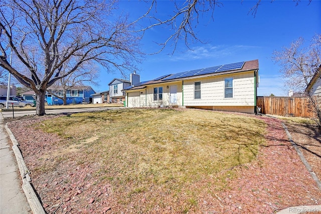 view of front of property featuring an attached garage, solar panels, a front lawn, and fence