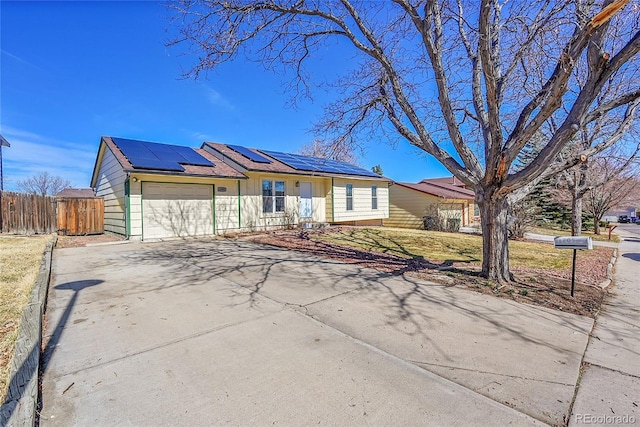 ranch-style house with roof mounted solar panels, concrete driveway, a garage, and fence